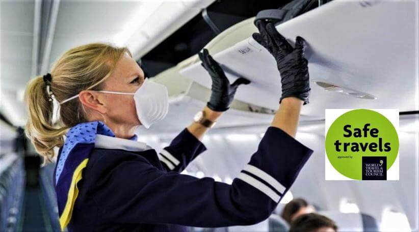 مهمانداری در هواپیما در حال بستن محفظه چمدان با دستکش و ماسک و رعایت پروتکل‌های بهداشتی در سفر